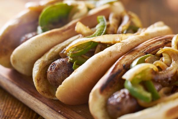 Brats with onions and peppers on top of them